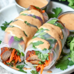 Close-up of fresh pork spring rolls with peanut lime sauce on a wooden platter.